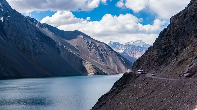 Camino de acceso al Embalse El Yeso bordeando la montaña, con vehículos circulando